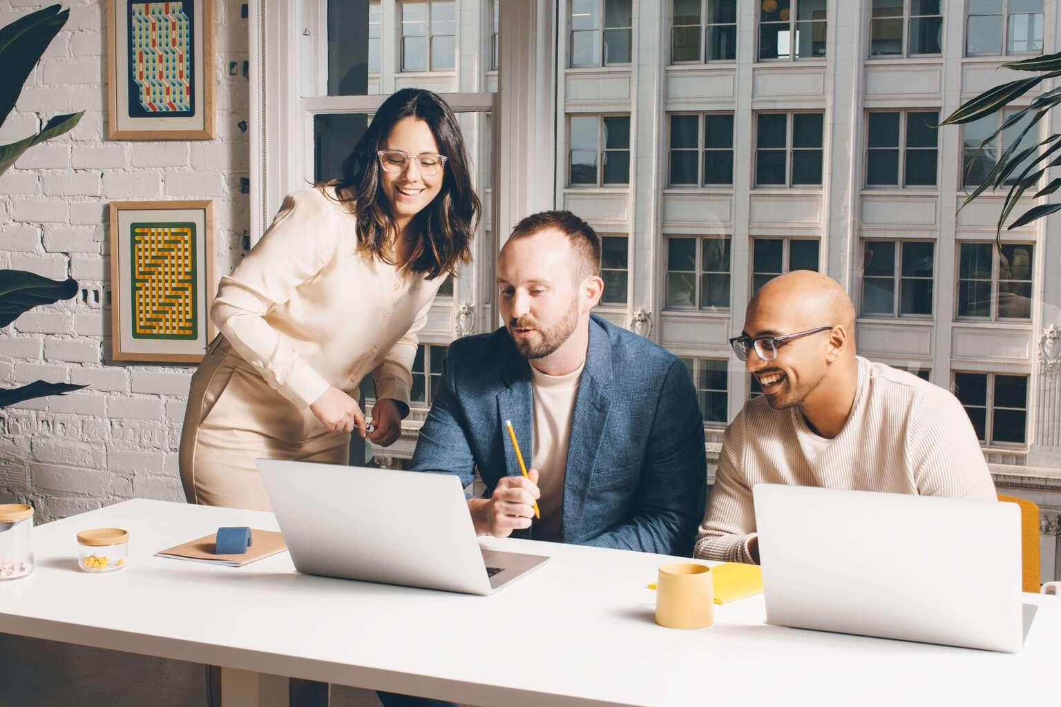 Image showing three coworkers collaborating around one person's laptop in an office environment